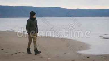 穿着暖和的衣服的男孩正沿着海滨的海岸走着，梦里梦里地看着水和山。